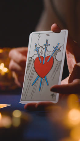 Vertical-Video-Close-Up-Of-Woman-Giving-Tarot-Card-Reading-On-Candlelit-Table-Holding-The-Devil-Card-2